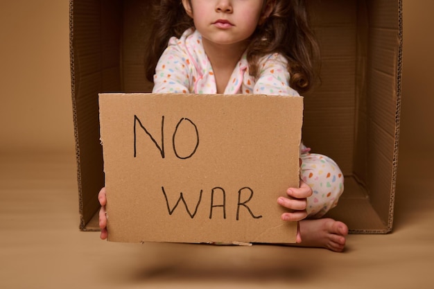 Sem guerra escrito em cartaz de papelão nas mãos de criança europeia refugiada ou migrante durante conflitos políticos e militares no país isolado sobre espaço de anúncio de cópia de fundo bege