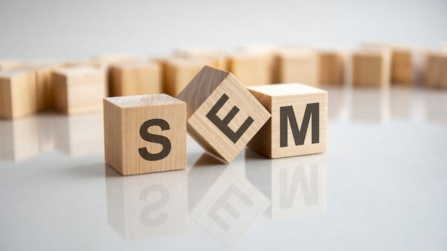SEM - Search Engine Marketing Akronymkonzept auf Würfeln, grauer Hintergrund. Reflexion auf der verspiegelten Oberfläche des Tisches. Selektiver Fokus.