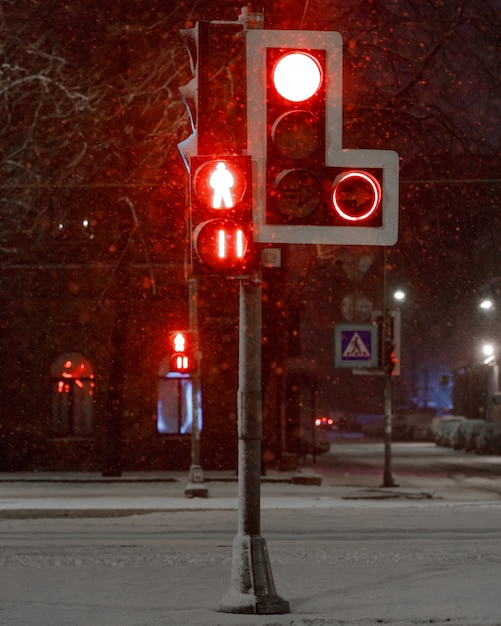 Semáforos con rojo para el transporte y los peatones durante una nevada en la noche. Señal de stop.