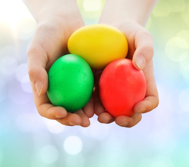 Semana Santa, vacaciones y concepto infantil - cierre de las manos de los niños sosteniendo huevos de colores sobre el fondo de las luces
