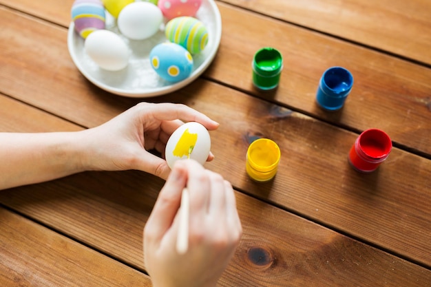 semana santa, vacaciones, tradición y concepto de la gente - cierre de manos de mujer coloreando huevos de pascua con colores y pincel