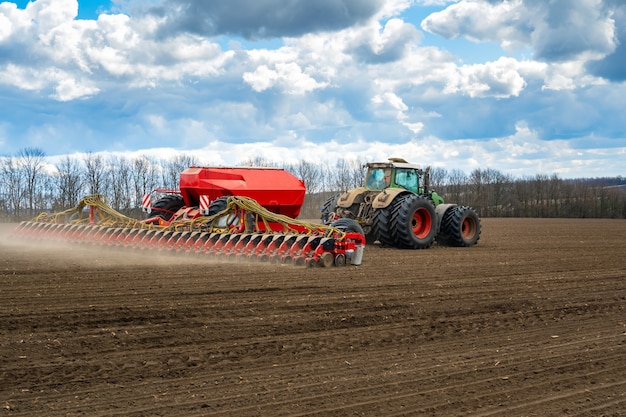 Semeando o trabalho no campo na primavera. Trator com semeadora.