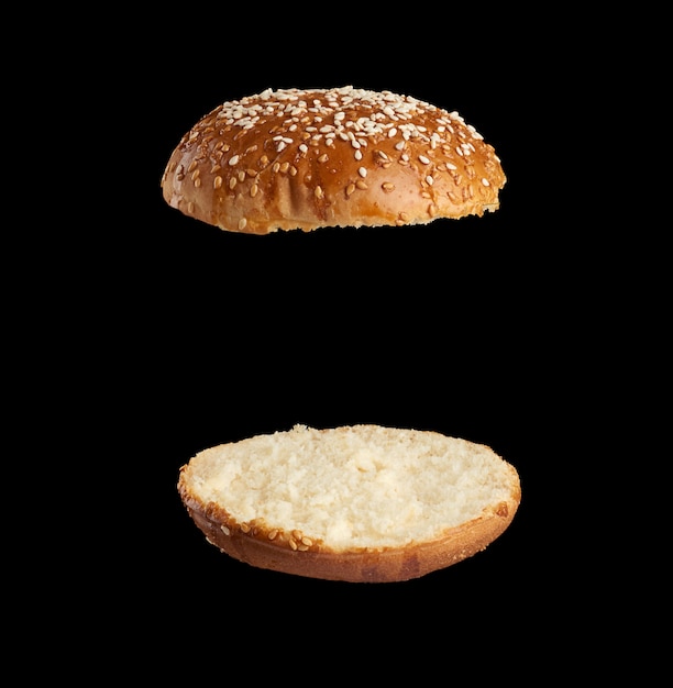 Semente de gergelim assado redondo com pãozinho cortado ao meio, as metades fritas e levitando uma sobre a outra, espaço preto