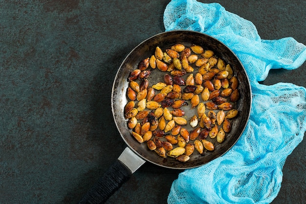 Sementes de abóbora fritas com temperos na frigideira de ferro velho Texturizado escuro