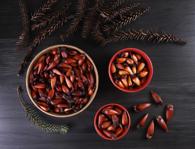 Sementes de araucária típicas usadas como condimento na culinária brasileira no inverno. Nozes de pinhão brasileiro em tigela de madeira marrom e vermelha sobre fundo cinza de madeira.