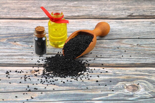 Foto sementes de cominho preto e óleo essencial com tigela e pá ou colher de madeira nigella sativa em garrafa de vidro medicamento herbal orgânico para muitas doenças