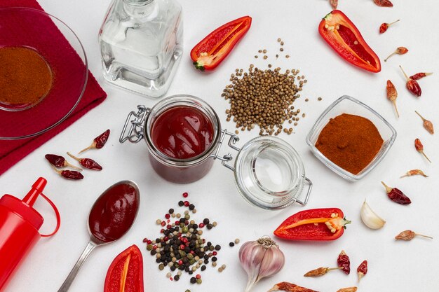 Sementes de pimenta da Jamaica e coentro na mesa. Molho de tomate na colher e na jarra. Metades de pimenta vermelha crua e vagens de pimenta seca. Vista do topo. Fundo branco.