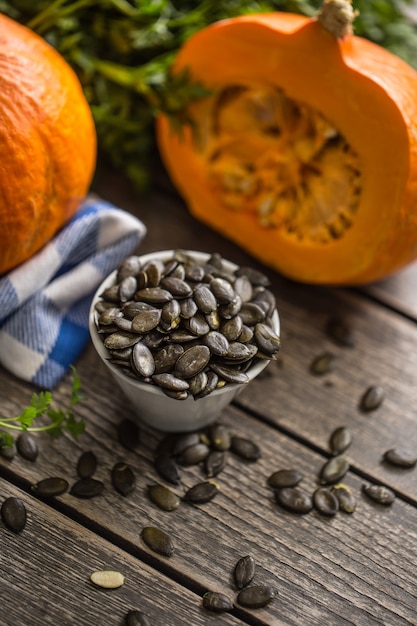 Semillas de calabaza tostadas con calabazas crudas en mesa de madera.