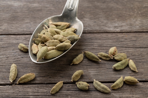 Semillas de cardamomo en una cuchara vieja sobre mesa de madera.