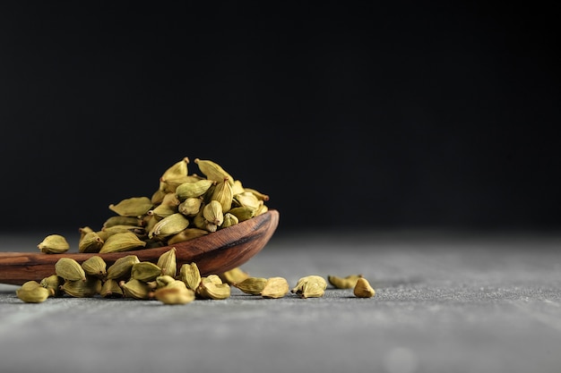 Semillas de cardamomo verde secas en una cuchara de madera sobre la mesa gris