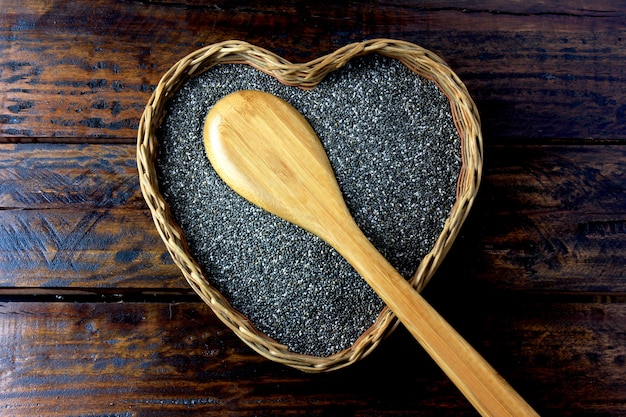 Semillas de Chia en la cesta con forma de corazón aislado en la mesa rústica junto a la cuchara. Vista superior