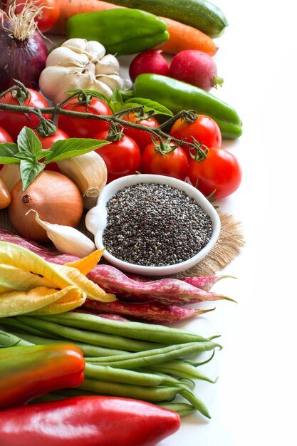 Semillas de chía crudas en un recipiente y verduras frescas aisladas en blanco de cerca