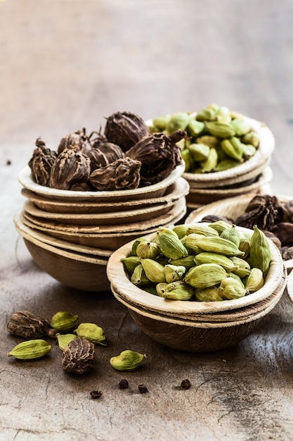 Semillas enteras de cardamomo negro y verde en tazones de coco en madera