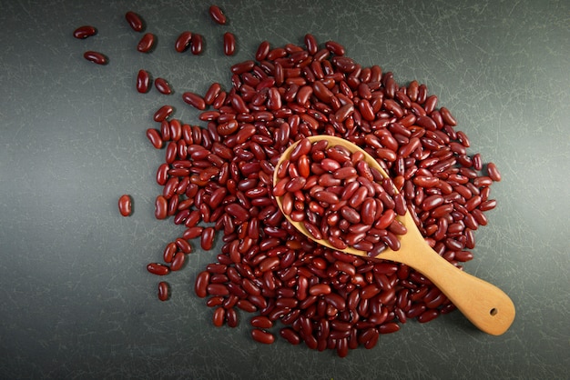 Semillas de frijoles rojos útiles para la salud en cucharas de madera sobre fondo gris.