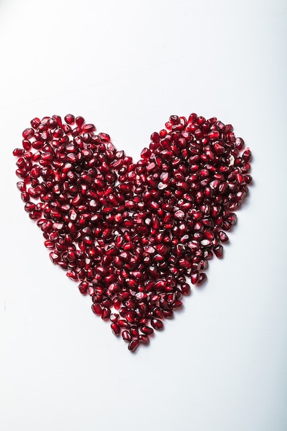 Foto semillas de granada en forma de corazón en blanco.