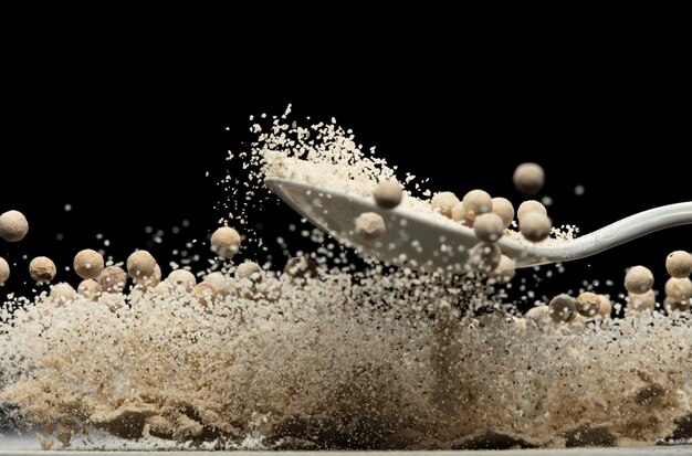 Las semillas de pimienta blanca explotan la explosión de la mezcla de pemienta blanca el polvo flota explotan las nubes abstractas la mosca de la mezclilla de pimientos el polvo salpica en el aire el fondo negro borrón de enfoque selectivo aislado