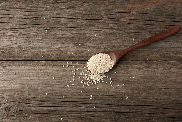 Semillas de sésamo blanco seco en una cuchara de madera marrón