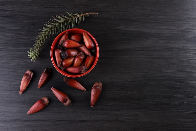 Semillas típicas de araucaria utilizadas como condimento en la cocina brasileña en invierno. Tuercas de piñón brasileño en cuenco de madera marrón y rojo sobre fondo de madera gris.