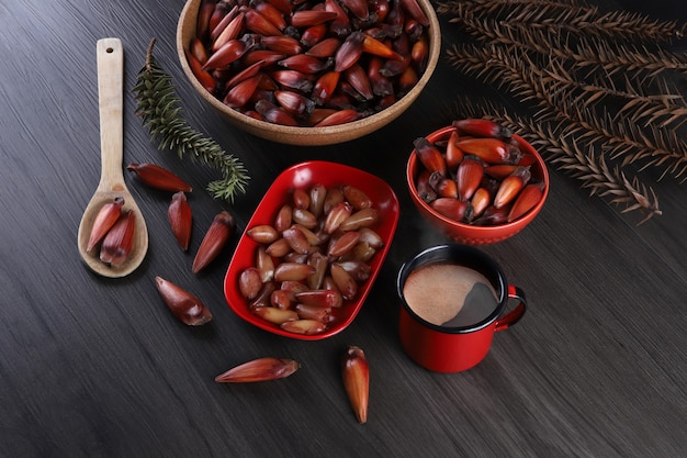 Semillas típicas de araucaria utilizadas como condimento en la cocina brasileña en invierno. Tuercas de piñón brasileño en cuenco de madera marrón y rojo sobre fondo de madera gris.