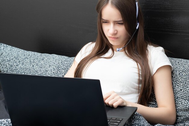 Seminario web de educación en línea Un estudiante en casa se dedica al entrenamiento escucha atentamente y ve una conferencia en una computadora portátil con un micrófono en los auriculares yace en la cama