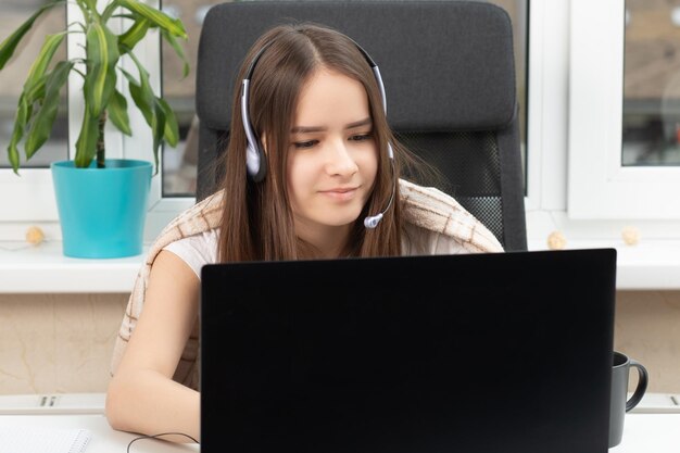 Seminario web de educación en línea Un estudiante en casa se dedica a la capacitación escucha atentamente y ve una conferencia en una computadora portátil con un micrófono en los auriculares