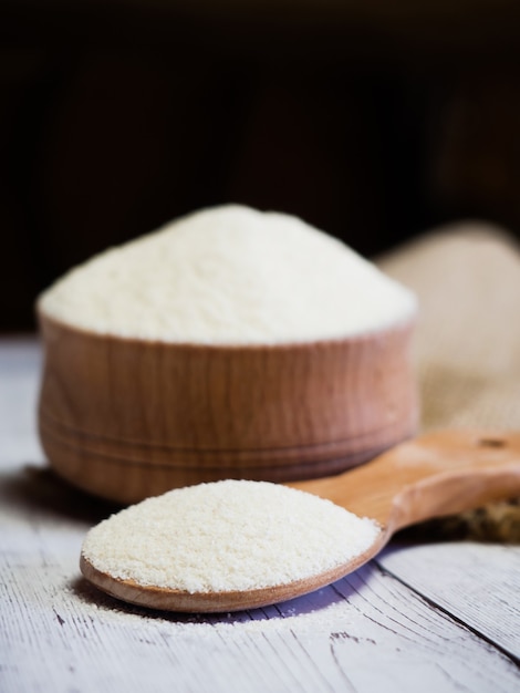 Sémola en un cuenco de madera y una cuchara sobre una mesa de madera blanca, primer plano. Fondo de cereales de dieta saludable.