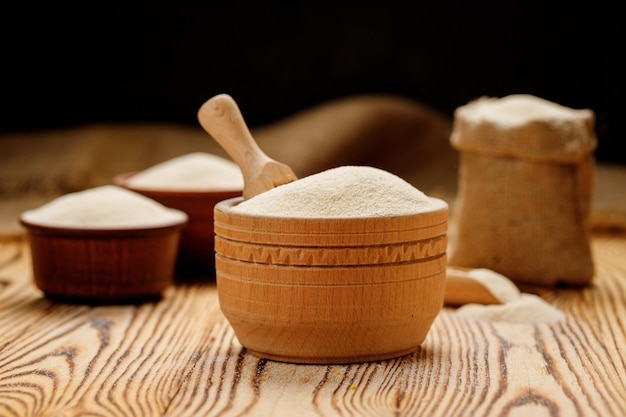 Semolina em tigelas e sacos em um fundo de madeira Foto de alta qualidade