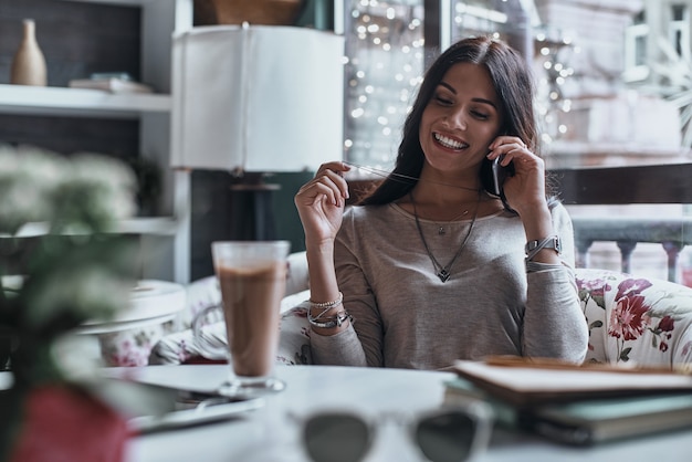 É sempre bom ouvir você! Mulher jovem e bonita sorrindo e falando ao telefone inteligente