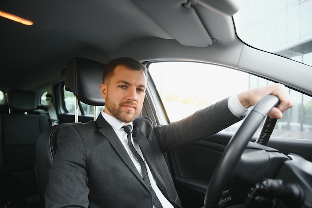 Sempre com pressa jovem bonito de terno completo sorrindo enquanto dirigia um carro