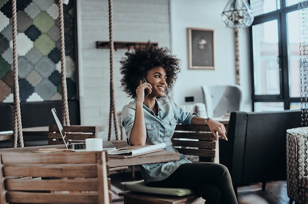 Sempre em contato com os clientes. Mulher jovem e bonita africana falando no telefone inteligente e sorrindo