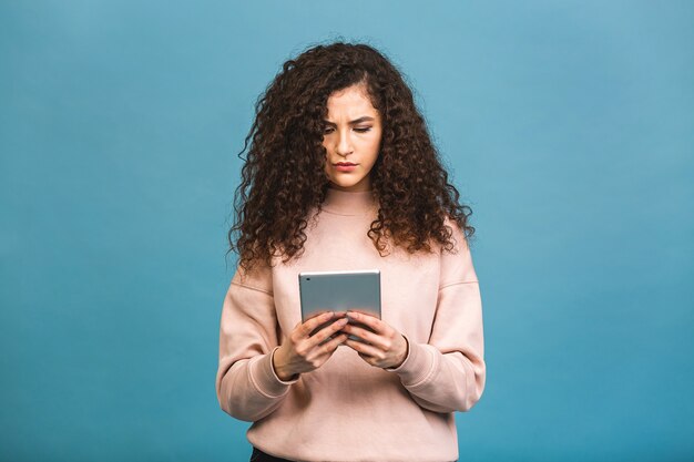 Sempre em contato! linda garota encaracolada sorrindo usando tablet isolado sobre fundo azul.