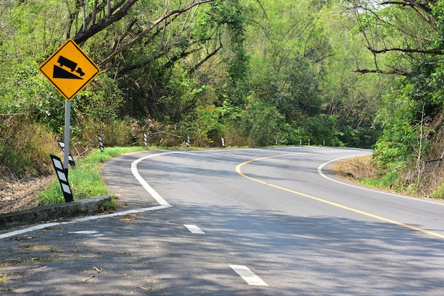 Señal de advertencia amarilla hermosa de la cuesta de la carretera de asfalto en el lado del país del bosque del midle