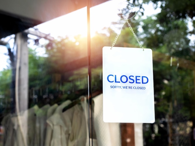 Señal de aviso blanco de cierre de la tienda con las palabras Lo siento estamos cerrados colgado en la puerta de vidrio frente a la tienda de ropa propietario de una pequeña empresa y concepto de servicios cerrados temporalmente