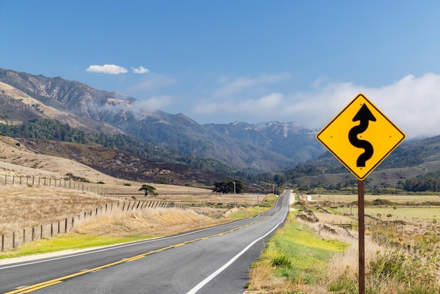 Señal de carretera de asfalto y paisaje campestre con cielo soleado