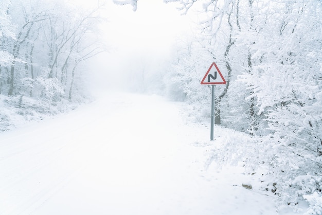 Señal de carretera sinuosa en carretera nevada