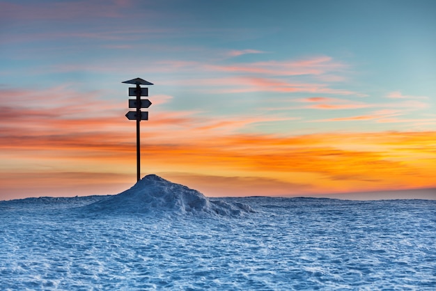 Señal de dirección en la cima de la montaña de invierno contra la puesta de sol