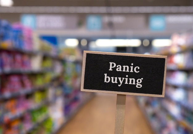 Foto señal de etiqueta de información de madera con texto compra de pánico contra el mensaje de los estantes de las tiendas desenfocado