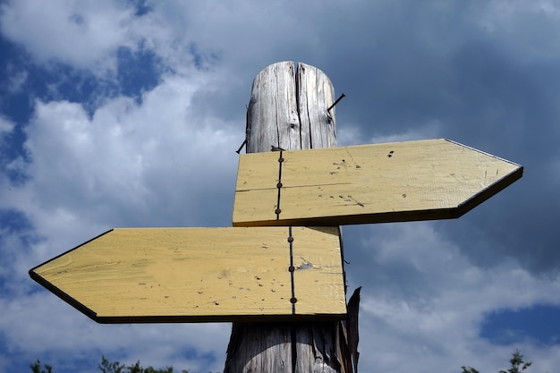 Señal de madera con dos flechas y cielo con nubes en el fondo