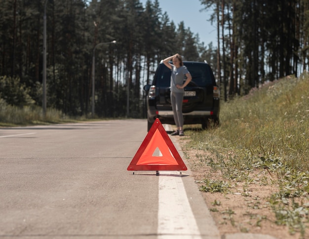 Señal de precaución triangular en la carretera después de la avería del coche y el conductor hablando por teléfono esperando una emergencia ...