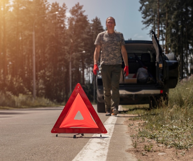 Señal de precaución de triángulo en la carretera cerca de un coche roto con el conductor caminando hacia él