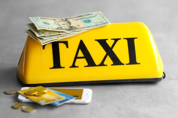 Señal de techo de taxi amarillo con tarjetas de crédito telefónicas y dinero en primer plano de fondo gris