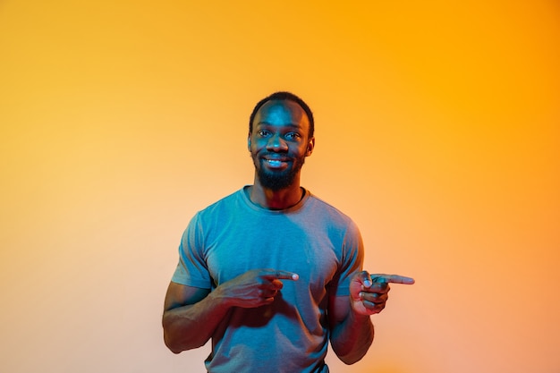 Señalando a un lado. Retrato moderno del hombre afroamericano en la pared del estudio anaranjado degradado