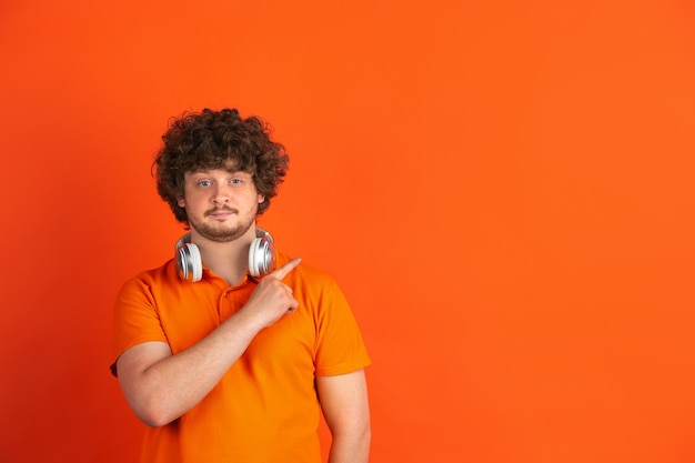 Foto señalar, elegir. retrato monocromático del hombre joven caucásico en la pared anaranjada. hermoso modelo masculino rizado en estilo casual. concepto de emociones humanas, expresión facial, ventas, publicidad.