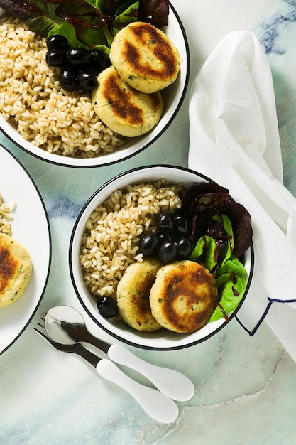 Un sencillo almuerzo o cena vegana para una familia de dos adultos y un niño arroz integral con okara de soja y empanadas de patata con ensalada fresca y aceitunas sobre una mesa de mármol