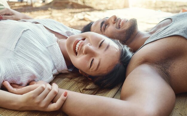 Foto senderismo, acampar y una pareja joven tirada en el suelo juntos al aire libre en la naturaleza para viajar o aventura amor sonrisa o libertad con una mujer asiática feliz y su novio vinculándose en el desierto