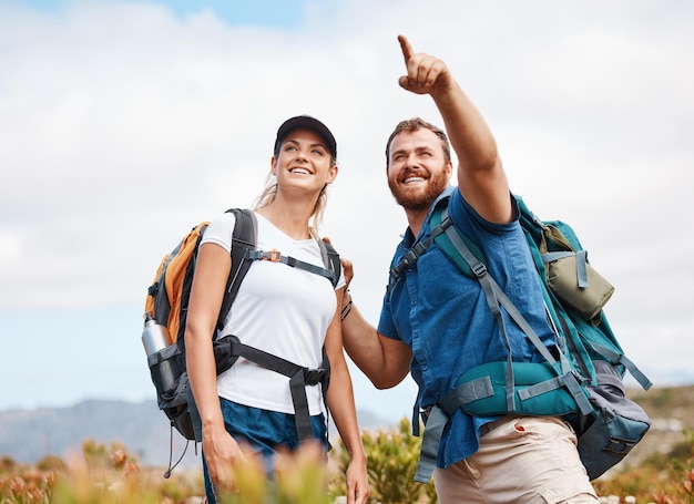 Senderismo feliz y pareja en la naturaleza relajarse y sonreír con la mano y señalar mientras habla y mira a su alrededor Amigos excursionistas y mujer con hombre en el bosque ejercicio cardiovascular y aventura al aire libre juntos