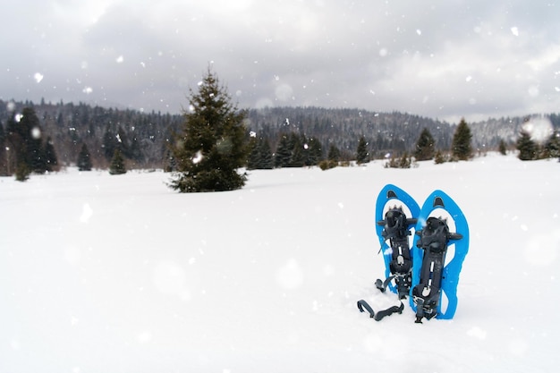 Senderismo de invierno en las montañas Raquetas de nieve azules en un espectáculo fresco con copos de nieve a su alrededor en un día de invierno nevado