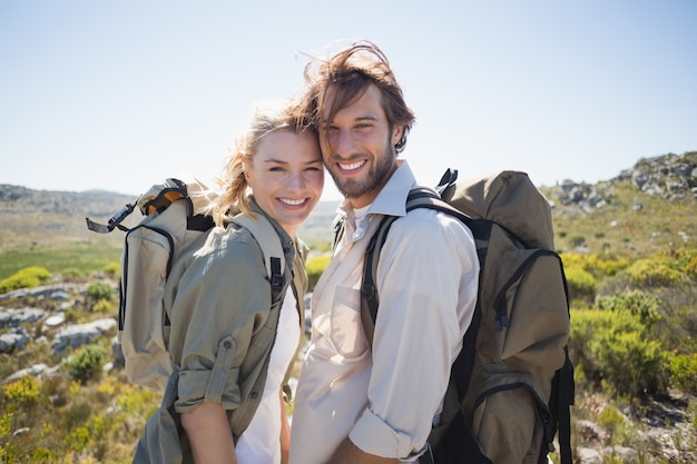 Senderismo pareja de pie en terreno de montaña sonriendo a la cámara