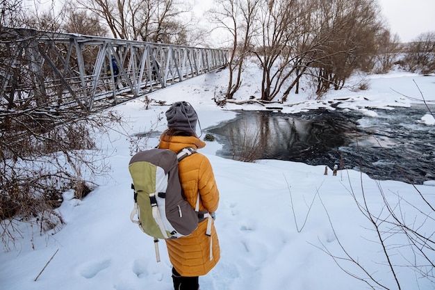 Senderismo turista está de pie ante el río con un puente Winter View