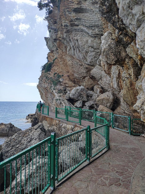 Foto sendero con valla cerca del mar y roca a la playa de mogren en budva montenegro
